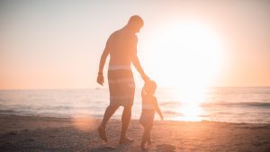 man and child walking on the beach at sunset