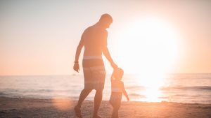 man and child walking on the beach at sunset